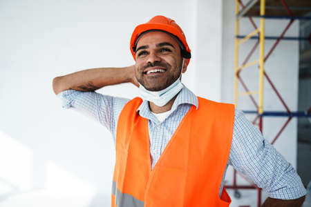 Portrait of mixed race man builder in workwear and hardhat wearing medical mask, close upの写真素材
