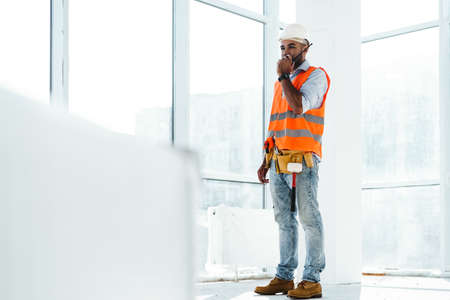 Young construction worker in uniform using walkie talkie on site