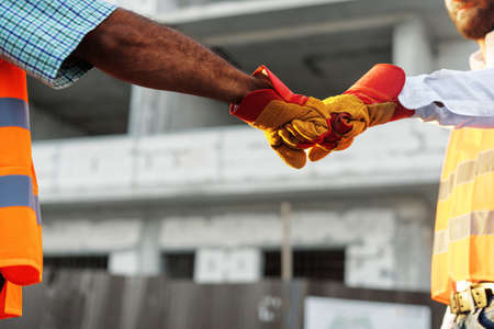 Two men engineers in workwear shaking hands against construction site.の写真素材