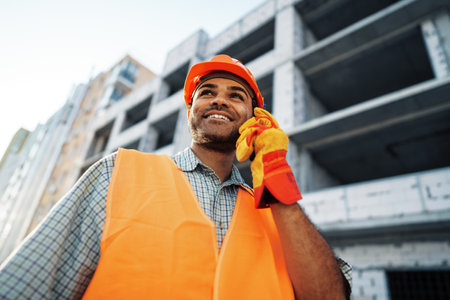 Young construction worker in uniform using walkie talkie on site