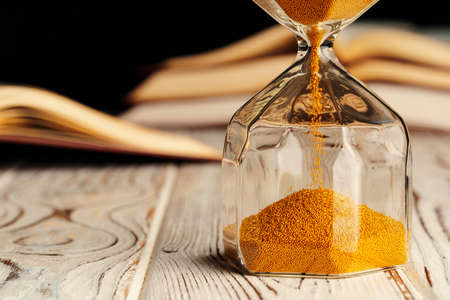 Sandglass on wooden table with opened book close upの写真素材