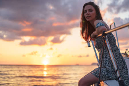Young attractive woman sitting on the deck of yacht and enjoying sunsetの写真素材