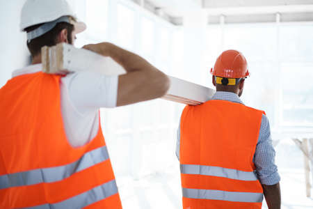 Two young men builders carrying wood planks on construction site, close upの写真素材