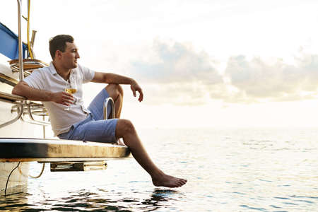 Young man holding a glass of wine on an open deck of a cruise boat