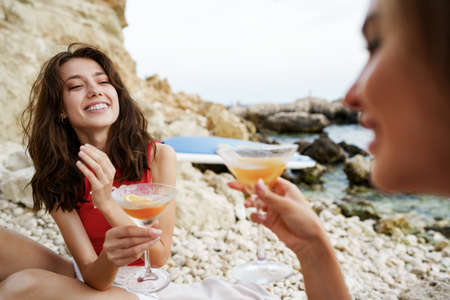 Two young female friends having picnic on a beach drinking cocktailsの写真素材
