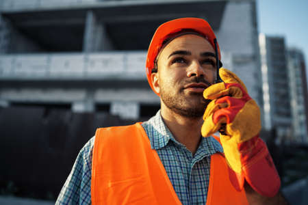 Young construction worker in uniform using walkie talkie on siteの写真素材