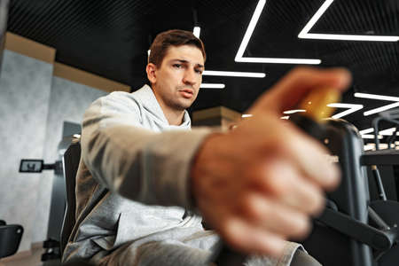 Young fit bodybuilder man doing arms workout training in the gym on machineの写真素材