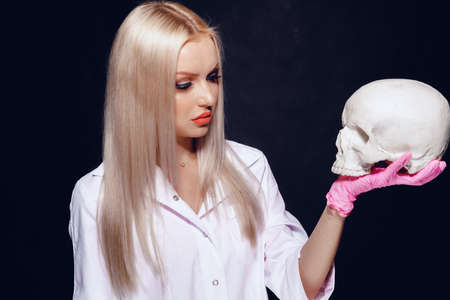 Woman doctor in medical uniform holding skull in hand on black backgroundの写真素材