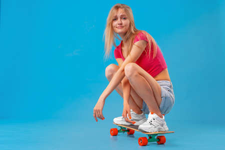 Pretty happy woman casually dressed sits on her skateboardの写真素材