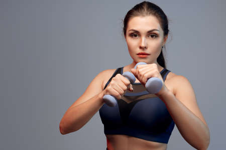 Portrait of a fitness model working out with dumbbells on grey backgroundの写真素材