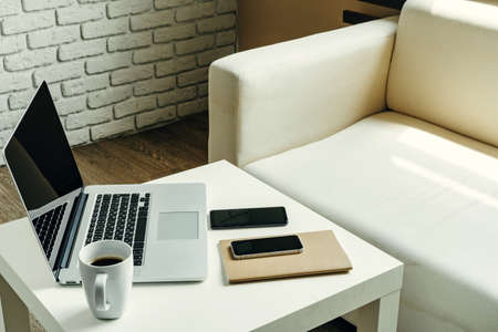 Open laptop on table near sofa, home interior. Freelancer workplace conceptの写真素材