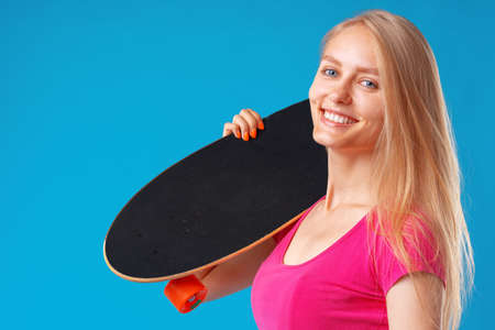 Attractive young woman holding her skateboard over blue background