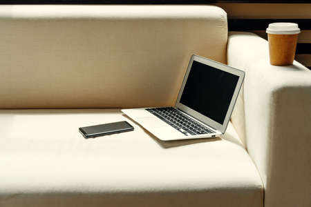 Open laptop on table near sofa, home interior. Freelancer workplace conceptの写真素材