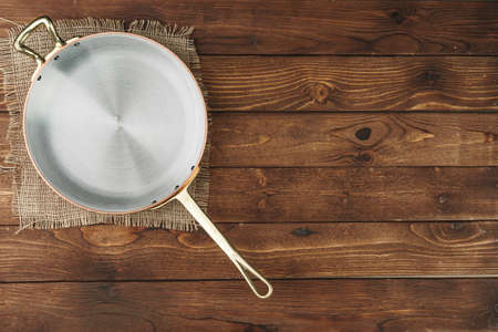 Copper frying pan on wooden background, top viewの写真素材