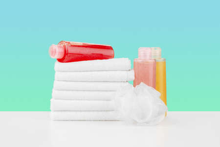 Pile of towels, bottles with shampoo on white tableの写真素材