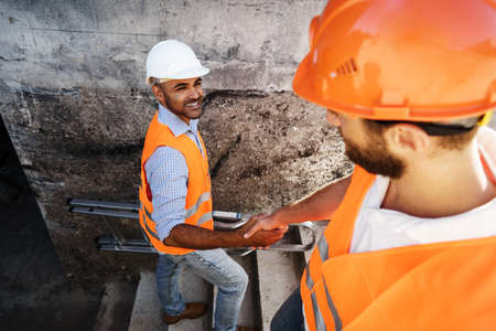 Two men engineers in workwear shaking hands against construction site.の写真素材