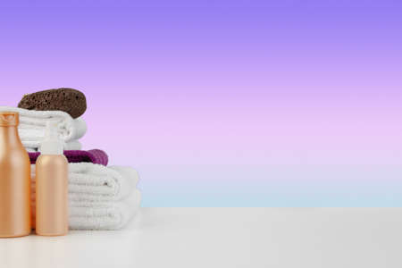 Pile of towels, bottles with shampoo on white tableの写真素材