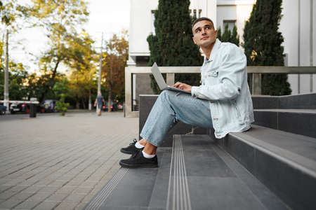 Young man sitting on stairs alone on street and working on laptopの写真素材
