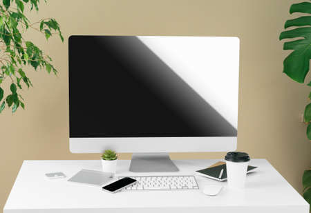 Stylish workspace with computer, keyboard, office supplies and plant in modern office