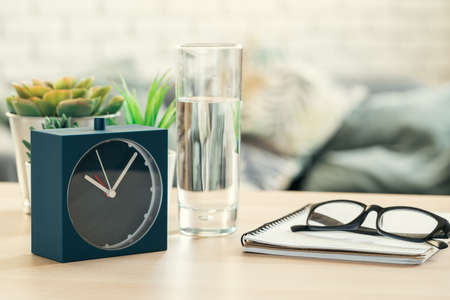 Drinking water health concept. Alarm clock and glass of water on table