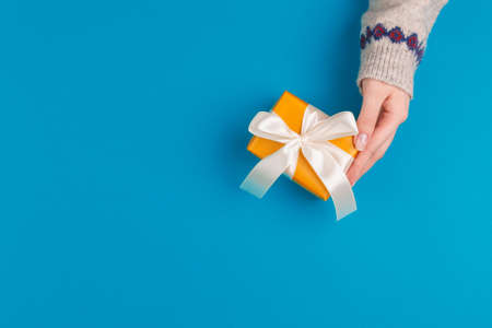 Small gift box in female hands on blue background, view from aboveの写真素材