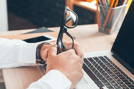Man sitting at desk at home and hold his glasses.の写真素材