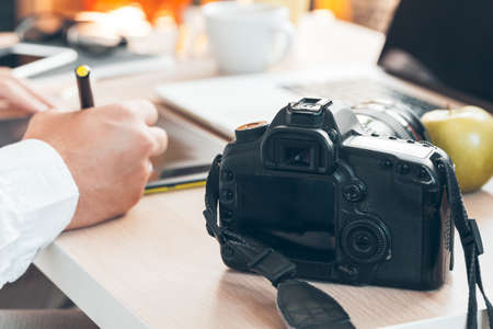 Young man photographer working on a computer. Work desk with keyboard, camera, laptop and lenses.の写真素材