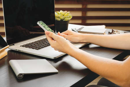 Smartphone with black screen in female hands. Computer, keyboard and office supplies on a backgroundの写真素材