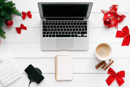 Laptop on white wooden desk surrounded with red Christmas decorations, top viewの写真素材
