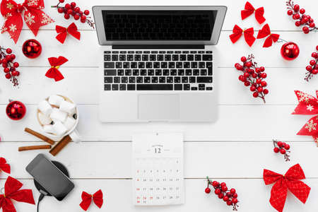 Laptop on white wooden desk surrounded with red Christmas decorations, top viewの写真素材