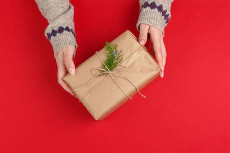 Female hands with christmas gift on red background, top view, copy space