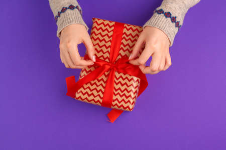 Female hands holding wrapped gift on purple backgroundの写真素材