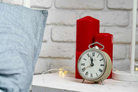 Metal vintage alarm clock standing on the nightstand near the bed close-upの写真素材