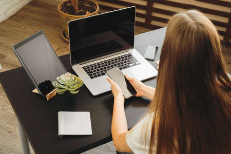 Smartphone with black screen in female hands. Computer, keyboard and office supplies on a backgroundの写真素材