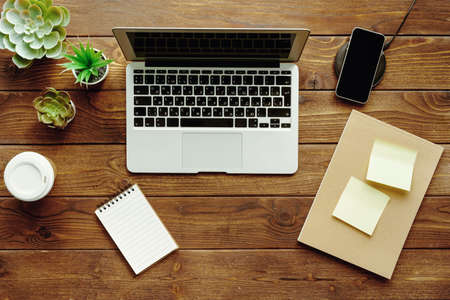 Office table workspace top view. Wooden desk with laptop, devices and plant