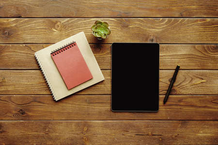 Digital tablet with black screen and notepad and pen on wooden table