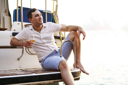 Young man holding a glass of wine on an open deck of a cruise boatの写真素材