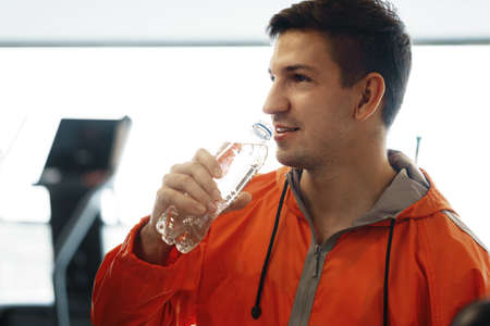 Portrait of young man drinking some water from a bottle in a gym