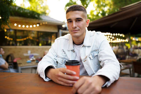 Young man with cup of coffee sitting in outdoor cafeの写真素材