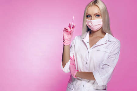 Doctor woman beautician standing with syringe against pink background and looking at cameraの写真素材