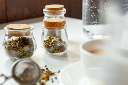 Glass jars with dry tea leaves close up on white tableの写真素材