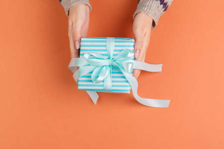Woman hands holding gift box on orange backgroundの写真素材