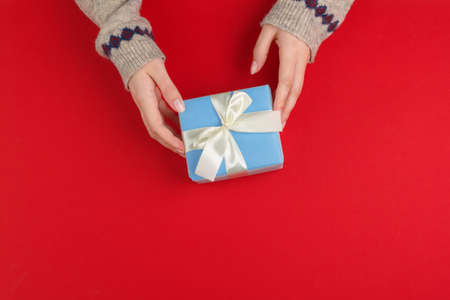 Female hands with christmas gift on red background, top view, copy spaceの写真素材
