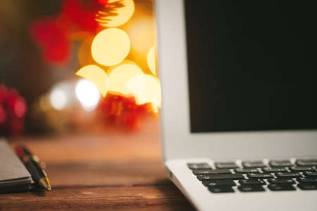 Wooden desk with computer with blank screen against blurred christmas lights backgroundの写真素材