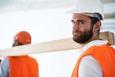 Two young men builders carrying wood planks on construction site, close up