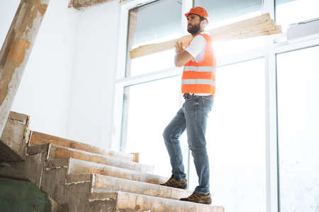 Builder man in hardhat carrying timber on building site, close up .