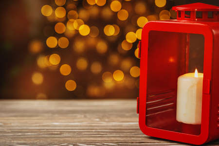 Christmas red lantern with burning candle on wooden tableの写真素材