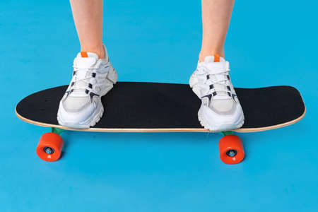 Teenager girl standing and posing on skateboard over a color background