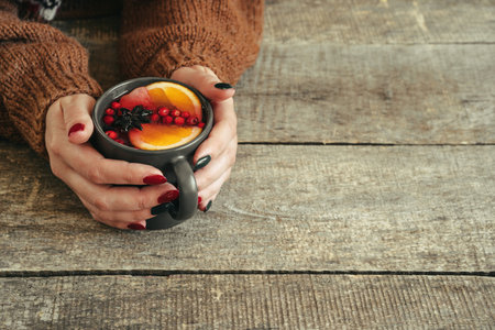 Womans hands in warm sweater holding a cup of mulled wineの写真素材