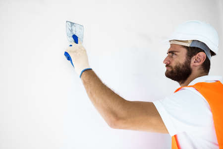 Plasterer in workwear smoothing wall surface of building indoorsの写真素材
